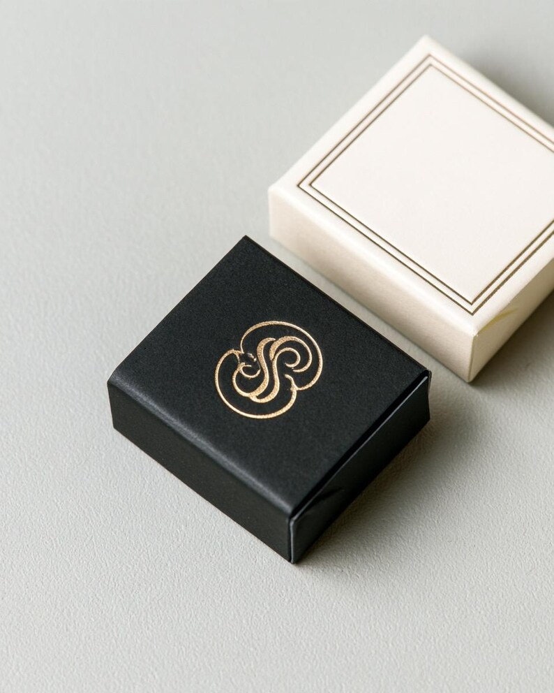 Small rectangular matchbox mockups in a restrained neutral palette, decorated with fine monograms. The styled arrangement shows the paper sleeves and drawer-style construction for personalised event favours.