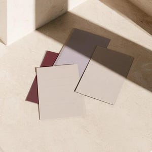 Layered unprinted menu-card mockups with curved paper edges in cream and muted burgundy tones. The arrangement shows contrasting paper shapes and soft shadows for a modern table-stationery design.