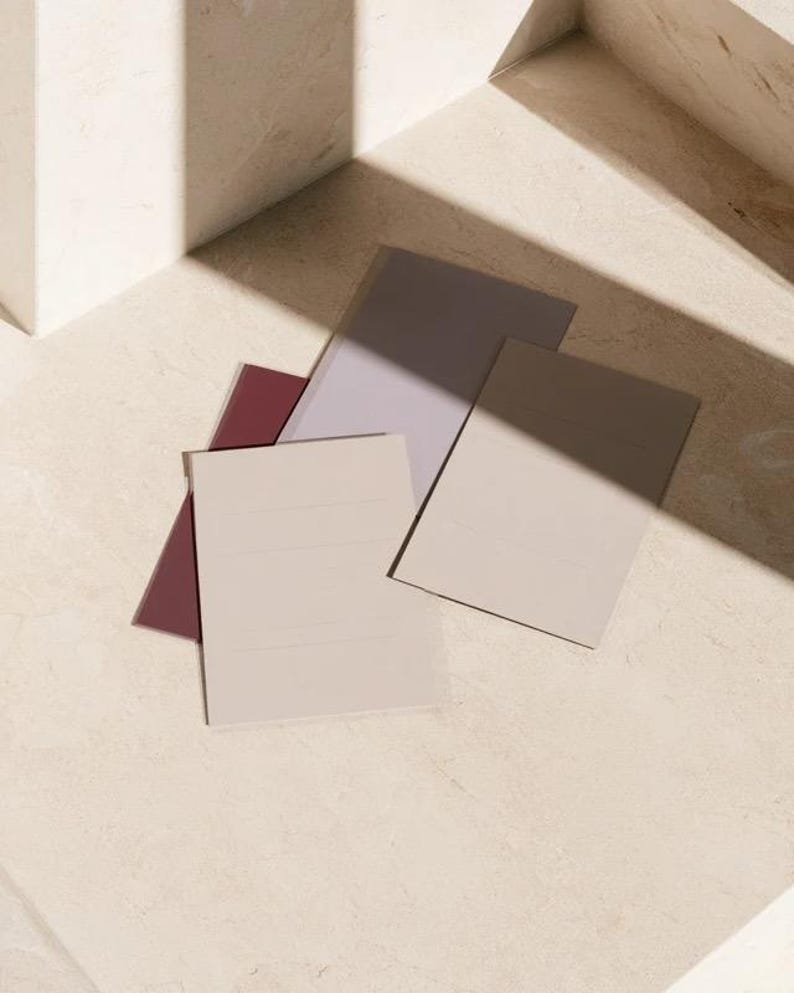 Layered unprinted menu-card mockups with curved paper edges in cream and muted burgundy tones. The arrangement shows contrasting paper shapes and soft shadows for a modern table-stationery design.