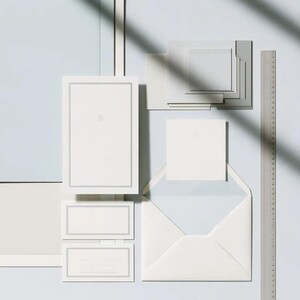 Unprinted cream invitation cards in several rectangular sizes with matching envelopes, arranged on a pale background. The mockup shows a coordinated wedding invitation, reply card and details-card format.