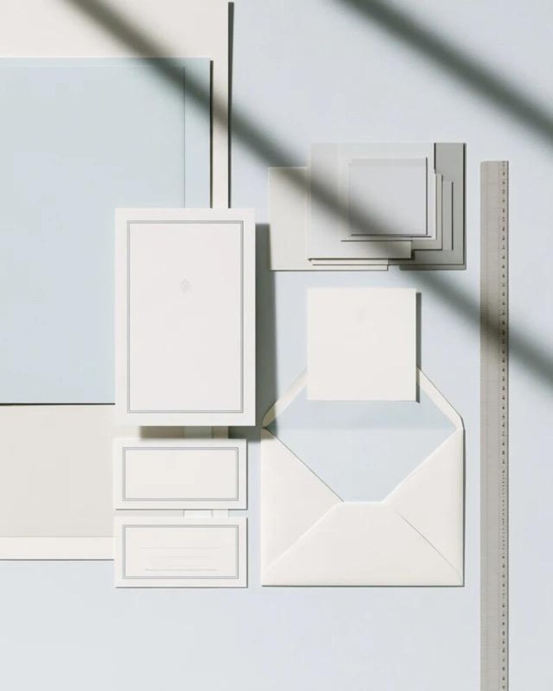 Unprinted cream invitation cards in several rectangular sizes with matching envelopes, arranged on a pale background. The mockup shows a coordinated wedding invitation, reply card and details-card format.