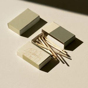 Cream rectangular drawer-style matchbox mockups arranged with coordinating neutral paper samples. The presentation shows sleeves, trays and the compact box proportions for bespoke event designs.