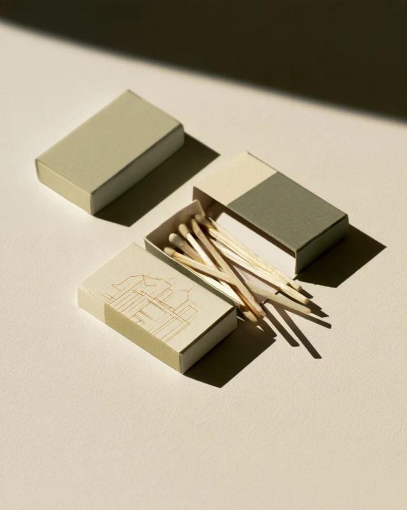 Cream rectangular drawer-style matchbox mockups arranged with coordinating neutral paper samples. The presentation shows sleeves, trays and the compact box proportions for bespoke event designs.