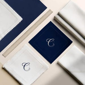 Square navy and cream cocktail napkins with small contrasting monogram letters, displayed with coordinating paper pieces. Digital concept mockup showing a personalised wedding or event table detail.