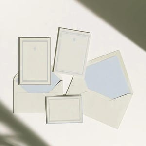Unprinted cream invitation cards in several rectangular sizes with matching envelopes, arranged on a pale background. The mockup shows a coordinated wedding invitation, reply card and details-card format.