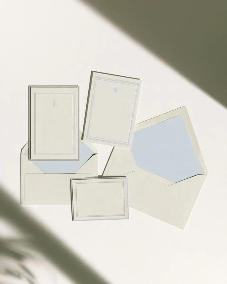 Unprinted cream invitation cards in several rectangular sizes with matching envelopes, arranged on a pale background. The mockup shows a coordinated wedding invitation, reply card and details-card format.