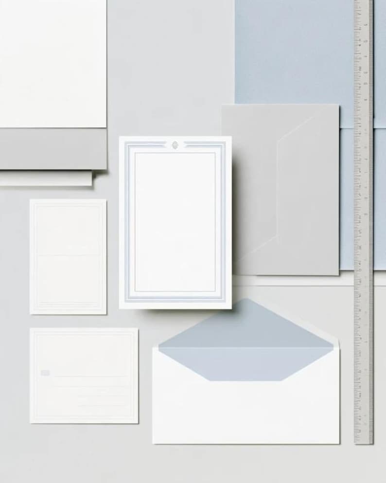 Unprinted cream invitation cards in several rectangular sizes with matching envelopes, arranged on a pale background. The mockup shows a coordinated wedding invitation, reply card and details-card format.