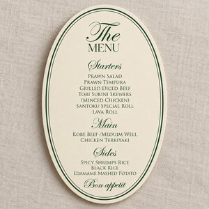 Może przedstawiać: Owalna karta menu w kolorze kremowym z ciemnozielonymi liniami brzegowymi i ciemnozielonym tekstem. Menu zawiera sekcje Starters, Main i Sides, w tym dania takie jak Prawn Salad, Grilled Diced Beef, Kobe Beef i Edamame Mashed Potato, kończąc się Bon appetit.