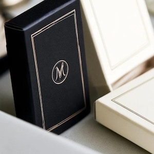 Small rectangular matchbox mockups in a restrained neutral palette, decorated with fine monograms. The styled arrangement shows the paper sleeves and drawer-style construction for personalised event favours.