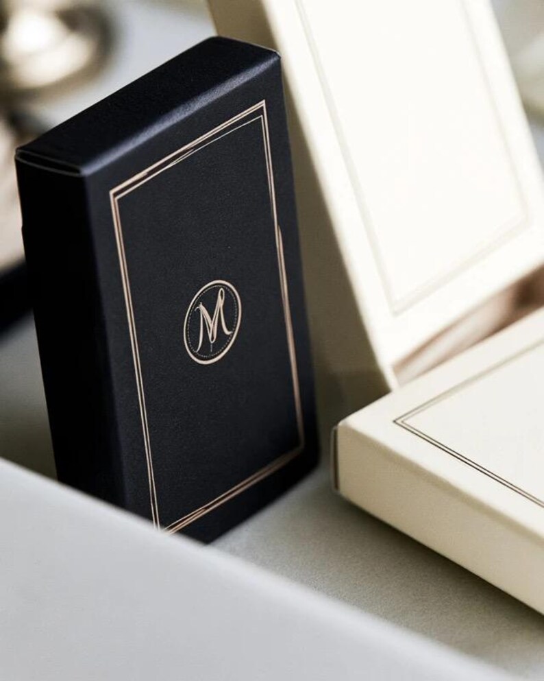 Small rectangular matchbox mockups in a restrained neutral palette, decorated with fine monograms. The styled arrangement shows the paper sleeves and drawer-style construction for personalised event favours.