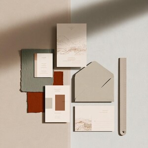 Coordinated wedding invitation stationery with cream cards, muted green accents and an envelope, arranged on a pale background. Fine architectural illustration and small printed text appear on the cards. Digital concept mockup.