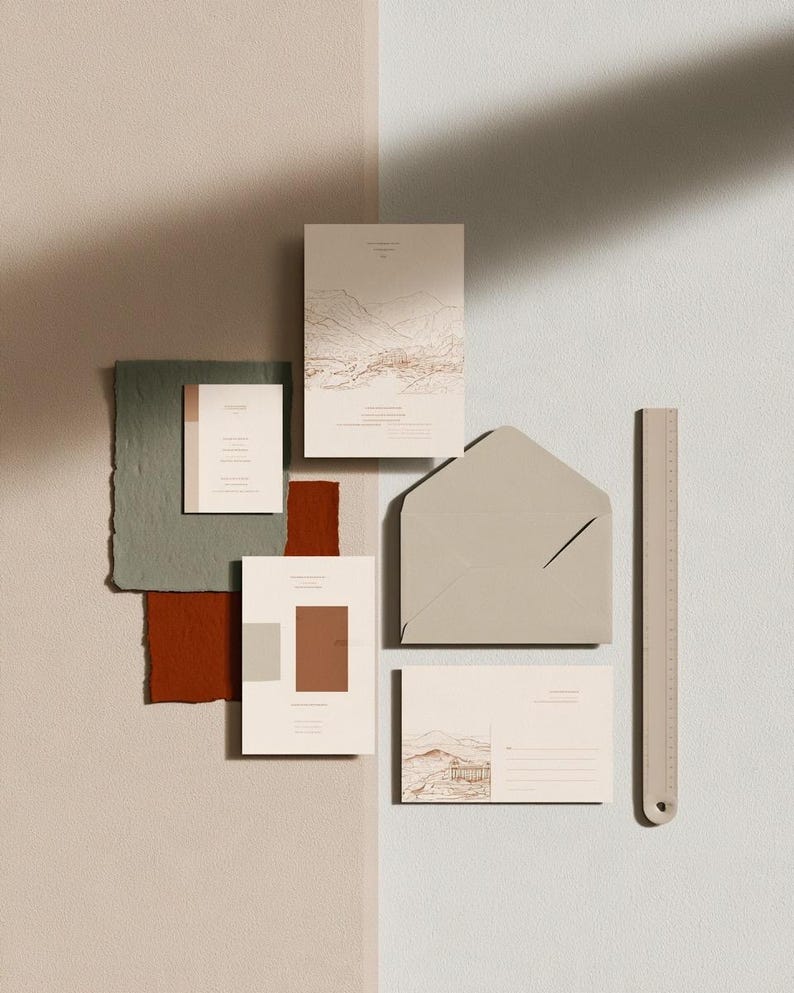 Coordinated wedding invitation stationery with cream cards, muted green accents and an envelope, arranged on a pale background. Fine architectural illustration and small printed text appear on the cards. Digital concept mockup.