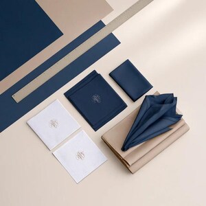 Square navy and cream cocktail napkins with small contrasting monogram letters, displayed with coordinating paper pieces. Digital concept mockup showing a personalised wedding or event table detail.