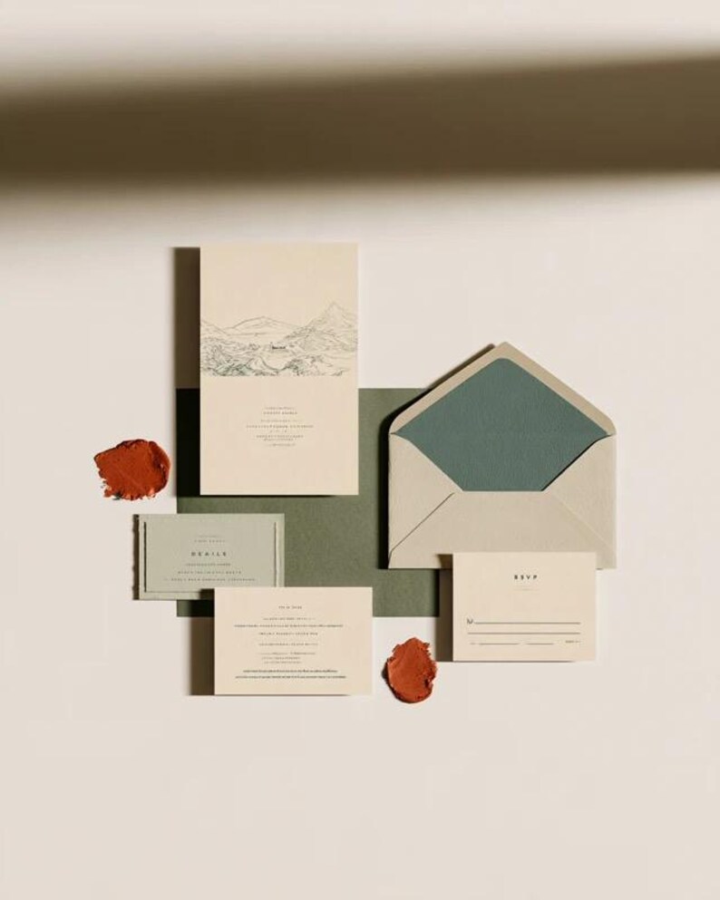 Coordinated wedding invitation stationery with cream cards, muted green accents and an envelope, arranged on a pale background. Fine architectural illustration and small printed text appear on the cards. Digital concept mockup.
