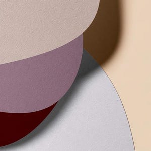 Layered unprinted menu-card mockups with curved paper edges in cream and muted burgundy tones. The arrangement shows contrasting paper shapes and soft shadows for a modern table-stationery design.