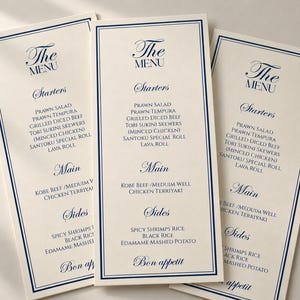 Może przedstawiać: Trzy wysokie, kremowe menu restauracyjne z ciemnoniebieskimi obw&oacute;dkami i eleganckim niebieskim tekstem. Menu zawierają sekcje Starters, Main i Sides, wymieniając dania takie jak Prawn Salad, Grilled Diced Beef i Chicken Teriyaki, kończąc się napisem Bon appetit.
