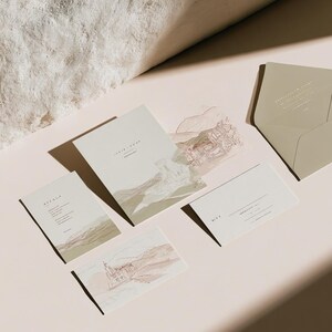 Coordinated wedding invitation stationery with cream cards, muted green accents and an envelope, arranged on a pale background. Fine architectural illustration and small printed text appear on the cards. Digital concept mockup.