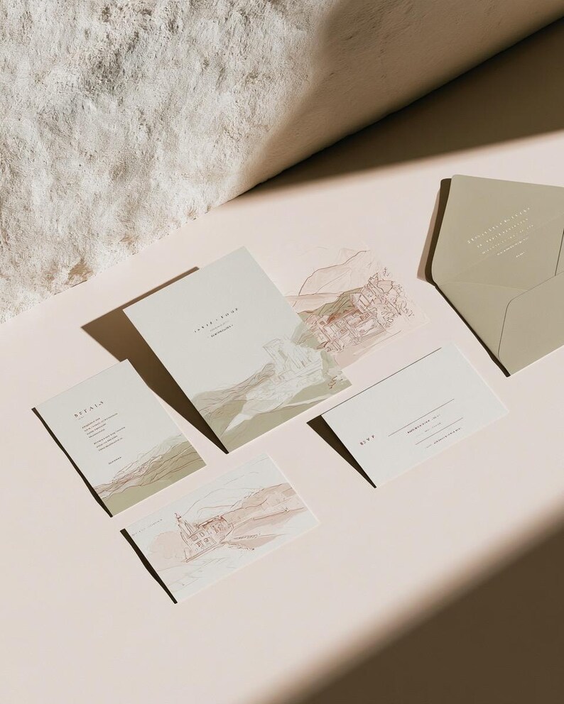 Coordinated wedding invitation stationery with cream cards, muted green accents and an envelope, arranged on a pale background. Fine architectural illustration and small printed text appear on the cards. Digital concept mockup.