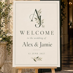 Ivory wedding welcome sign on a wooden easel, with a dark green AJ monogram, botanical details and the sample wording Alex & Jamie, 12 June 2027. Digital design mockup; easel is a styling prop.