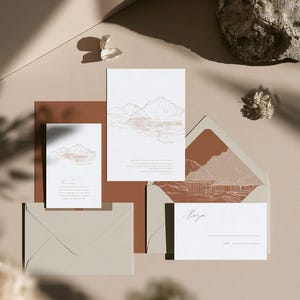 Coordinated wedding invitation stationery with cream cards, muted green accents and an envelope, arranged on a pale background. Fine architectural illustration and small printed text appear on the cards. Digital concept mockup.