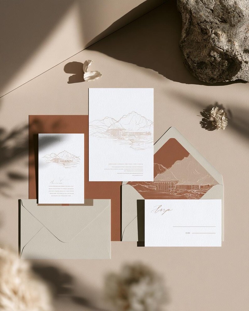 Coordinated wedding invitation stationery with cream cards, muted green accents and an envelope, arranged on a pale background. Fine architectural illustration and small printed text appear on the cards. Digital concept mockup.