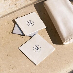 Square navy and cream cocktail napkins with small contrasting monogram letters, displayed with coordinating paper pieces. Digital concept mockup showing a personalised wedding or event table detail.