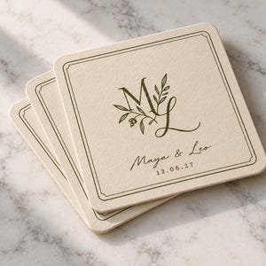 Digital studio mockup of three thin ivory square paper coasters with rounded corners, arranged in an offset stack on pale marble. Olive-green ML monogram, fine frame and matching Maya and Leo wording.