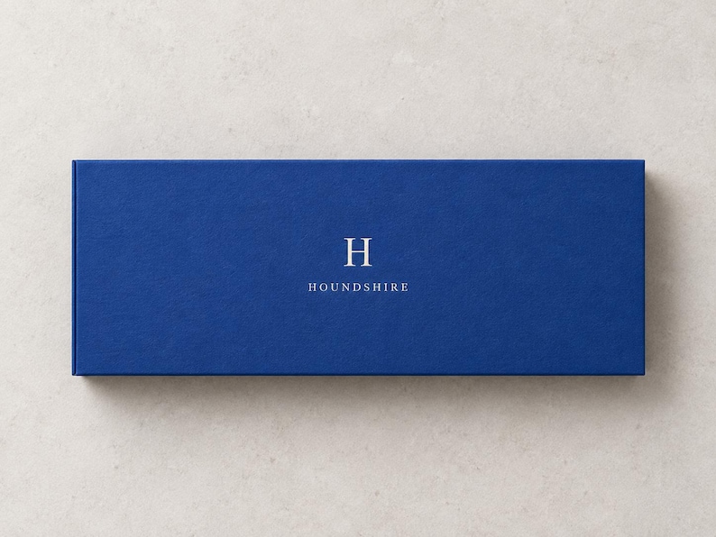 AI-assisted studio illustration of the closed 28 x 10.5 x 3 cm blue matchbox, shown from above with an ivory Houndshire sample monogram. The 28 cm measurement is the outside box length.