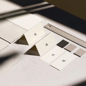 Cream wedding place cards with small dark initials and fine lettering, shown as flat and folded cards on a pale surface. Digital concept mockup of personalised table stationery.