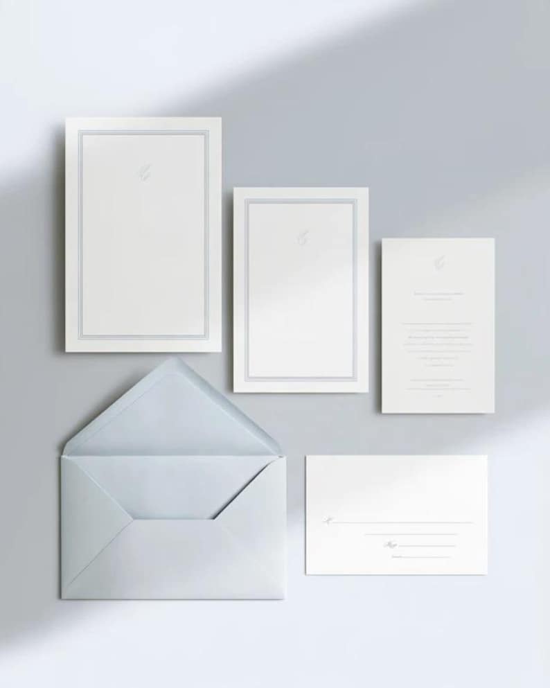 Unprinted cream invitation cards in several rectangular sizes with matching envelopes, arranged on a pale background. The mockup shows a coordinated wedding invitation, reply card and details-card format.