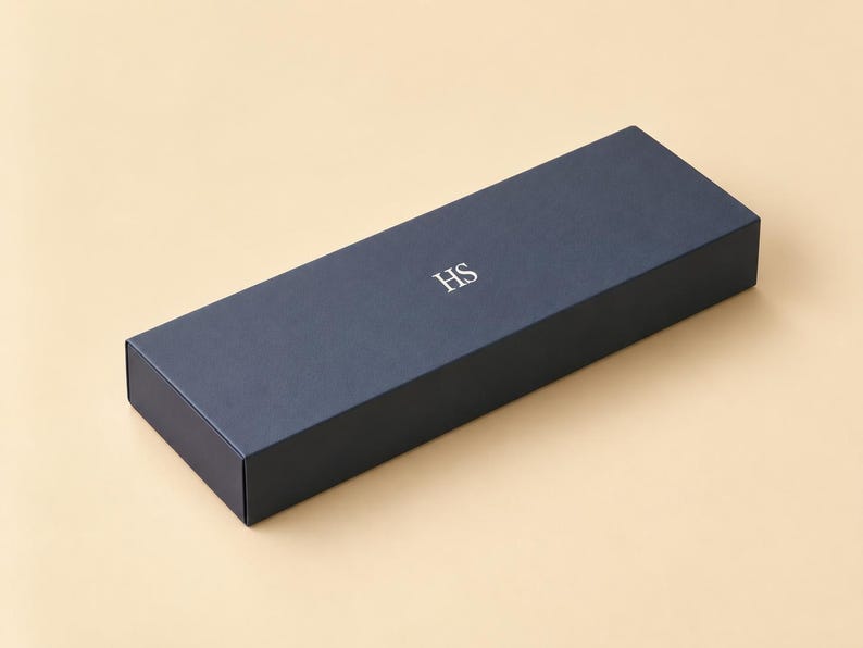 AI-assisted studio design visual of a closed navy sliding matchbox with an example HS monogram, on an ivory background. Illustrates the 28 x 10.5 x 3 cm outside box format; the monogram is an example, not a supplied design.