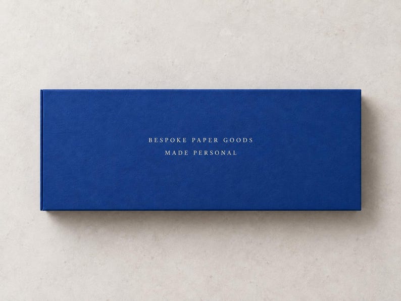 AI-assisted studio illustration of the reverse of the blue 28 cm matchbox, with ivory sample wording: Bespoke Paper Goods, Made Personal.
