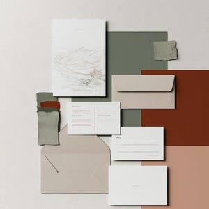 Coordinated wedding invitation stationery with cream cards, muted green accents and an envelope, arranged on a pale background. Fine architectural illustration and small printed text appear on the cards. Digital concept mockup.