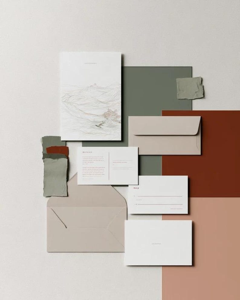 Coordinated wedding invitation stationery with cream cards, muted green accents and an envelope, arranged on a pale background. Fine architectural illustration and small printed text appear on the cards. Digital concept mockup.