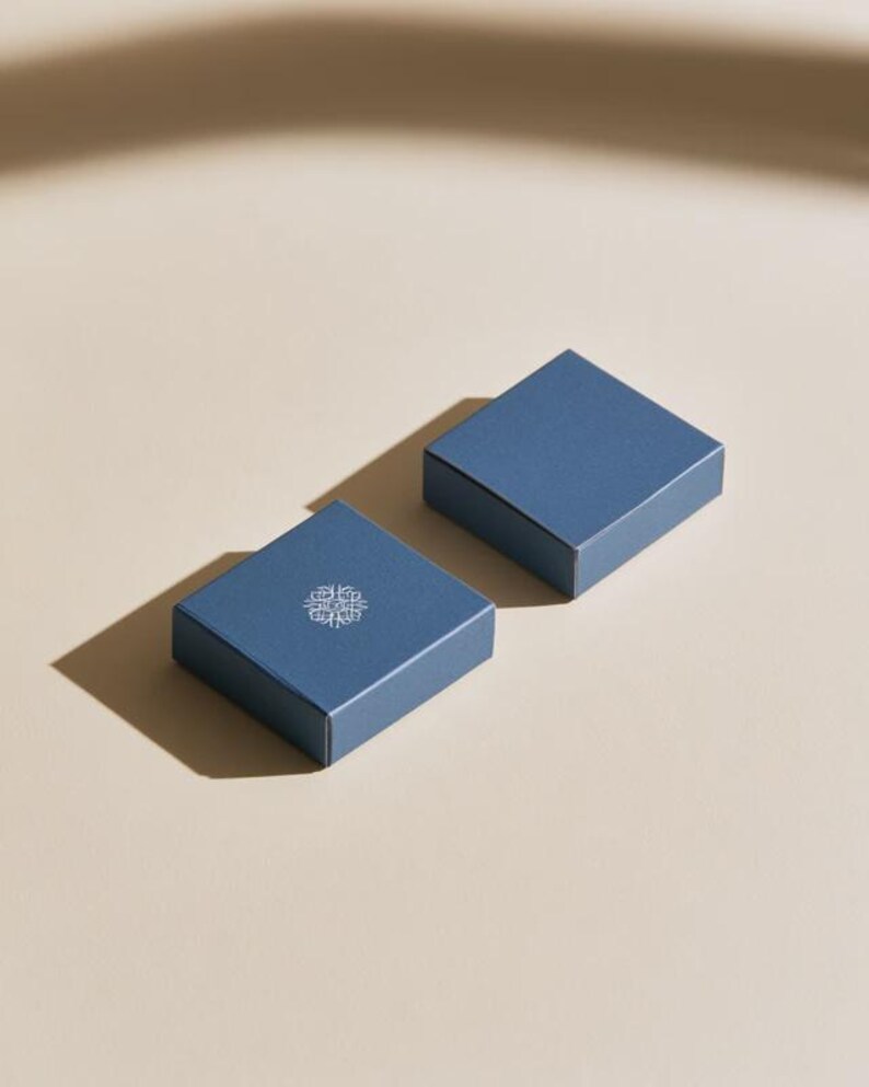 Contemporary matchbox mockup with a coloured paper sleeve and a clean graphic layout. The rectangular box is presented in soft directional light as a personalised wedding or event favour concept.