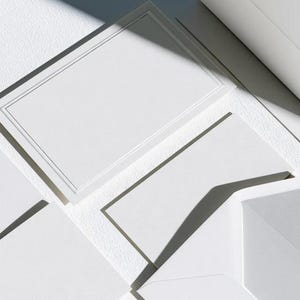 Unprinted cream invitation cards in several rectangular sizes with matching envelopes, arranged on a pale background. The mockup shows a coordinated wedding invitation, reply card and details-card format.