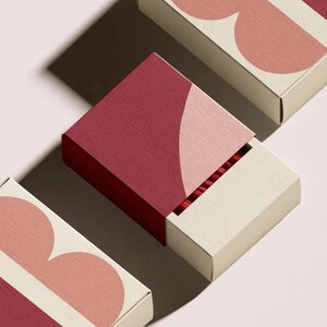 Contemporary matchbox mockup with a coloured paper sleeve and a clean graphic layout. The rectangular box is presented in soft directional light as a personalised wedding or event favour concept.