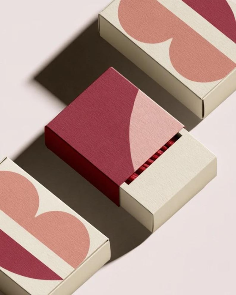 Contemporary matchbox mockup with a coloured paper sleeve and a clean graphic layout. The rectangular box is presented in soft directional light as a personalised wedding or event favour concept.