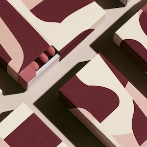 Contemporary matchbox mockup with a coloured paper sleeve and a clean graphic layout. The rectangular box is presented in soft directional light as a personalised wedding or event favour concept.