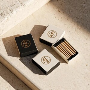 Small rectangular matchbox mockups in a restrained neutral palette, decorated with fine monograms. The styled arrangement shows the paper sleeves and drawer-style construction for personalised event favours.