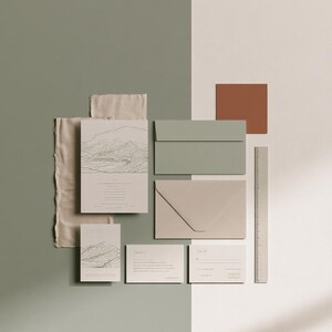 Coordinated wedding invitation stationery with cream cards, muted green accents and an envelope, arranged on a pale background. Fine architectural illustration and small printed text appear on the cards. Digital concept mockup.