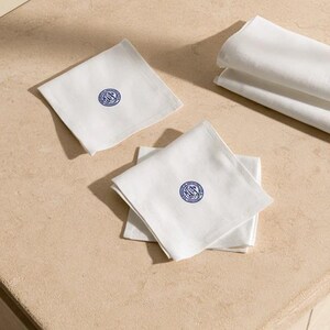 Square navy and cream cocktail napkins with small contrasting monogram letters, displayed with coordinating paper pieces. Digital concept mockup showing a personalised wedding or event table detail.