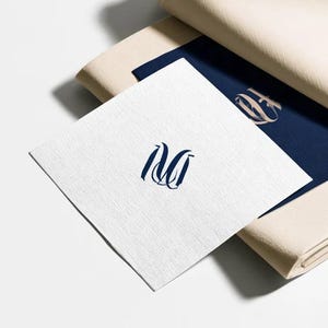 Square navy and cream cocktail napkins with small contrasting monogram letters, displayed with coordinating paper pieces. Digital concept mockup showing a personalised wedding or event table detail.