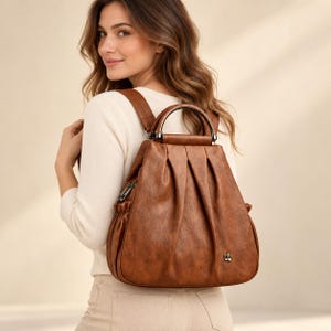 Puede incluir: Una mochila de aspecto de cuero marrón con un asa superior redondeada, pliegues verticales en el panel frontal y un pequeño emblema metálico en forma de flor en la parte inferior. La bolsa incluye bolsillos laterales fruncidos y cremalleras plateadas.
