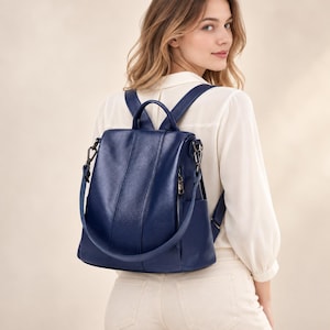 Puede incluir: Una mochila azul oscuro con acabado texturizado, que cuenta con un asa superior, correas ajustables para los hombros y un compartimento vertical con cremallera en la parte frontal. La bolsa incluye bolsillos laterales y herrajes metálicos.