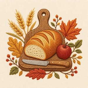 May include: An embroidery design featuring a loaf of sliced bread on a wooden cutting board with a knife, surrounded by wheat stalks, a red apple, and autumn leaves in shades of orange, yellow, and green on a cream-colored fabric background.