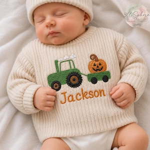 May include: A cream-colored ribbed knit sweater featuring an embroidered green tractor pulling a trailer with an orange jack-o'-lantern pumpkin. The name Jackson is embroidered in orange thread below the tractor design. The sweater has long sleeves.
