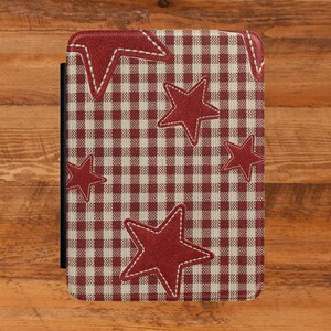 May include: A rectangular e-reader case featuring a red and beige gingham check pattern. The surface is decorated with several five-pointed red stars, each outlined with white stitching. The case has a black spine visible on the left side.