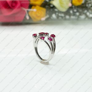 Peut inclure: Une bague argent&eacute;e dot&eacute;e d'un design &agrave; tige fendue orn&eacute;e de cinq pierres pr&eacute;cieuses rouges vibrantes en forme de poire. Les pierres sont dispos&eacute;es en grappe sur le dessus de l'anneau, cr&eacute;ant une structure ajour&eacute;e distincte au fini poli.