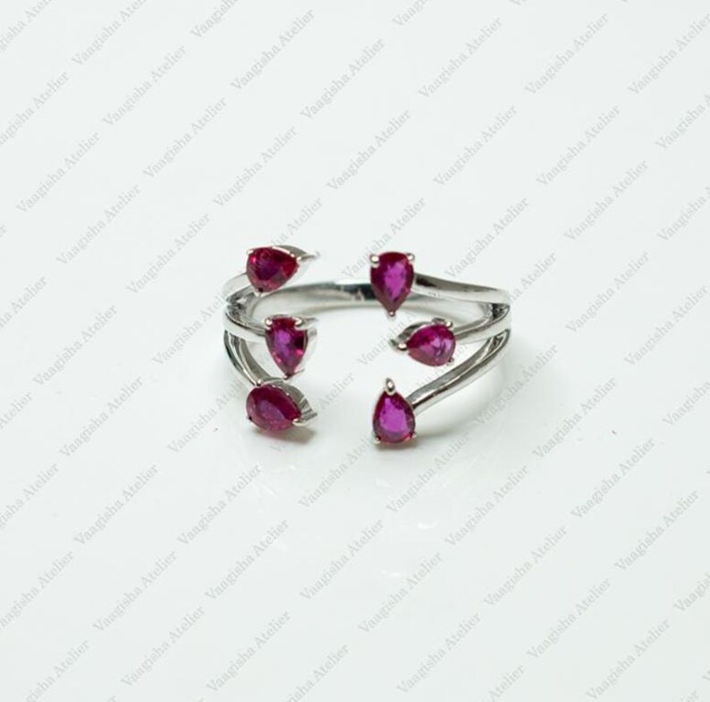 Peut inclure: Une bague ouverte argent&eacute;e orn&eacute;e de cinq pierres en forme de poire d'un rouge ros&eacute; profond, dispos&eacute;es le long de l'anneau fendu. Le design comprend trois pierres d'un c&ocirc;t&eacute; et deux de l'autre, cr&eacute;ant une esth&eacute;tique sym&eacute;trique et ouverte.